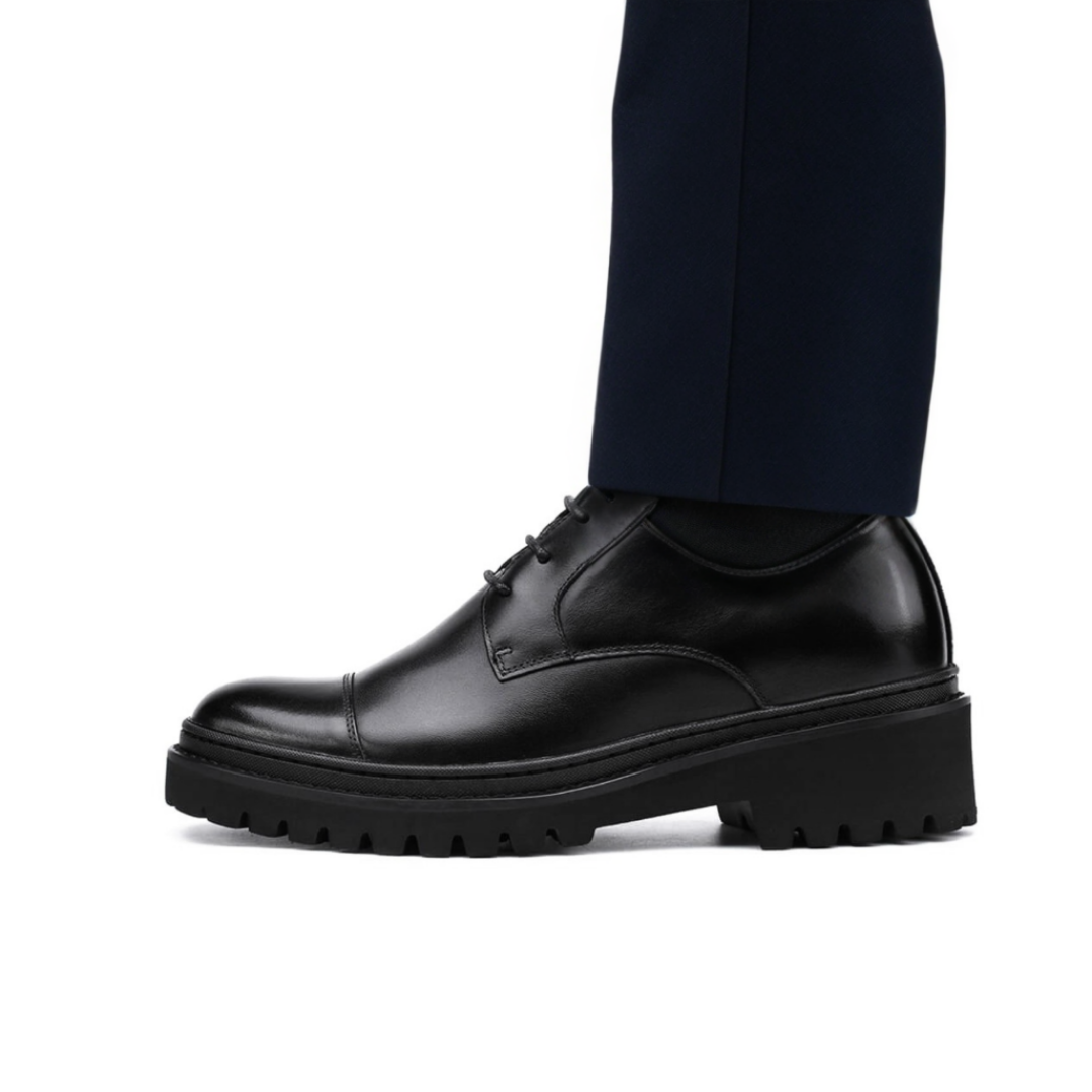 Black leather shoe worn with navy pants on a white background